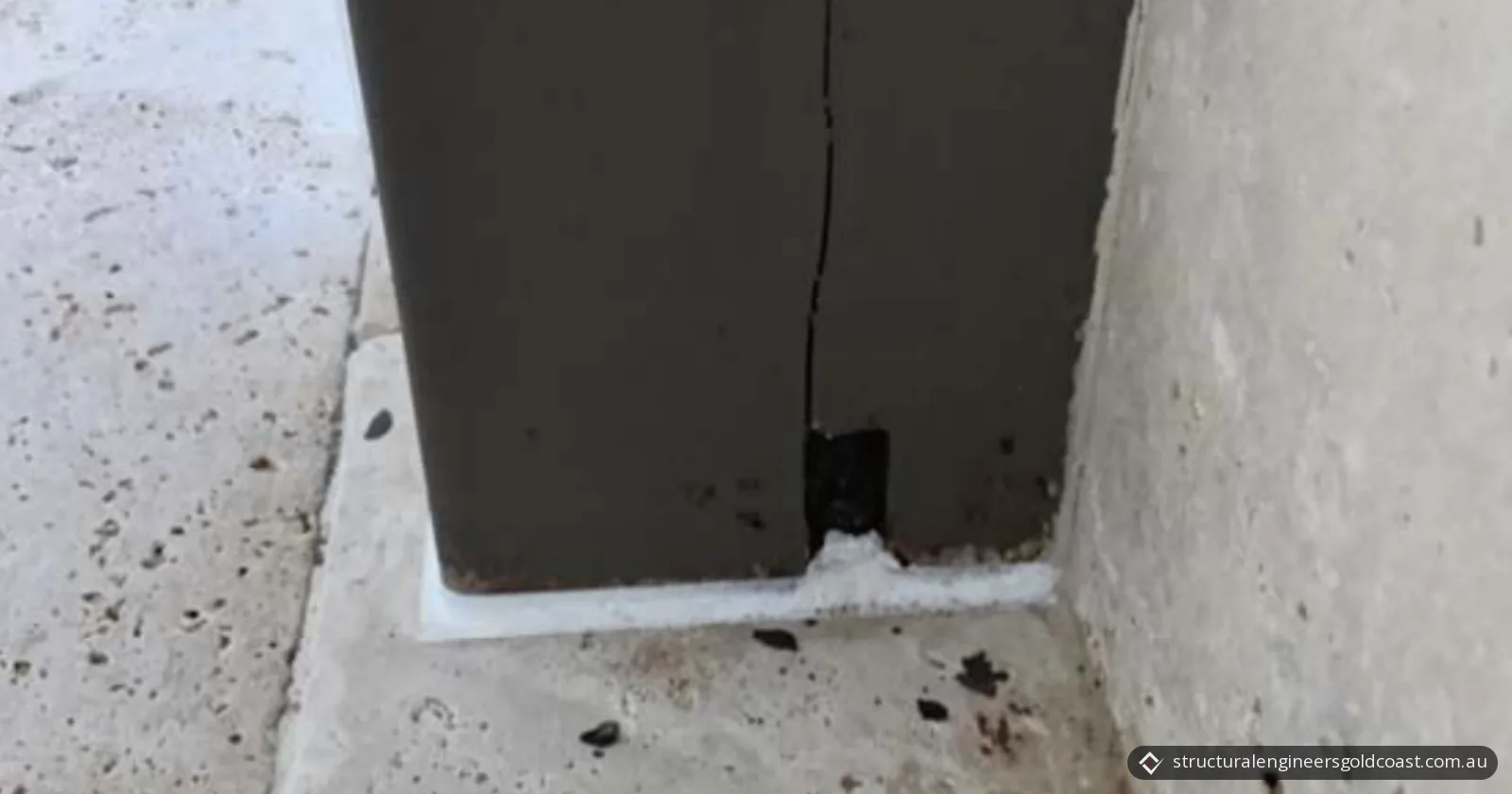 Base of a dark-painted hardwood post on stone paving, with a vertical crack running up from the steel base plate connection at its foot