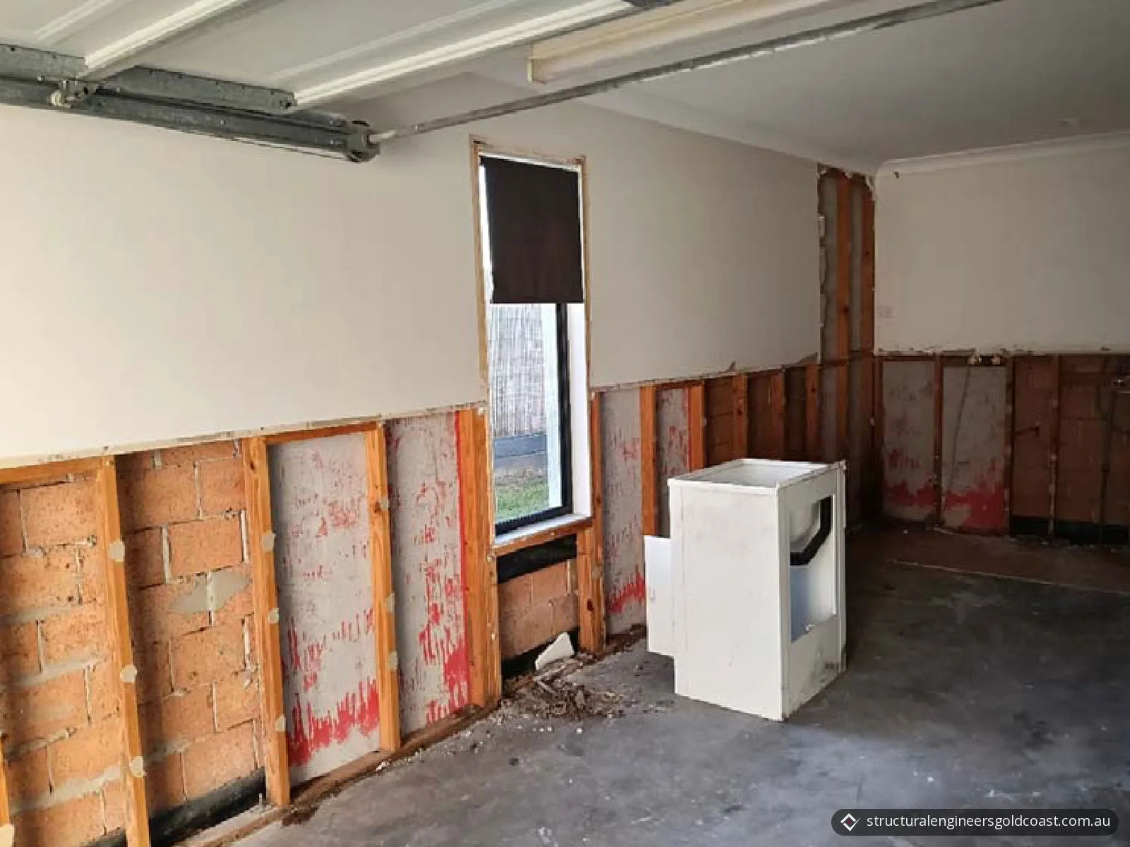 Garage with the lower wall lining removed, showing timber studs, masonry blocks and debris along the base of the wall