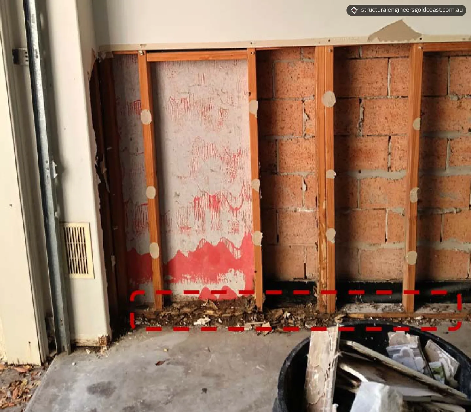 Base of a timber stud wall where the bottom plate has crumbled into debris, marked with a red dashed box